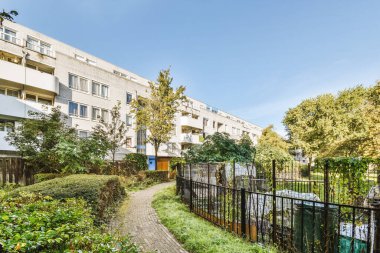 Güneşli bir günde arka planda bazı bitki ve binaların olduğu bir dış alan, sanki yaz mevsimiymiş gibi.