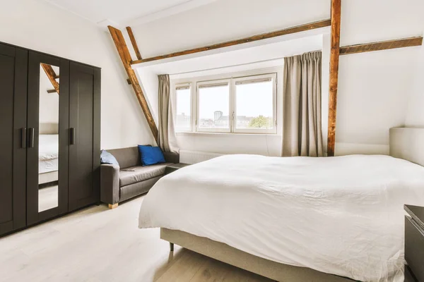 a bedroom with white bedding and wooden beams on the ceiling in front of the room is a large window
