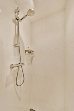 Beyaz fayanslı bir banyoda, duvarları siyah döşemeli ve duvara yapıştırılmış bir duş.