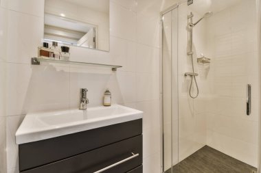 Duvarlarında siyah beyaz fayanslar olan modern bir banyo. Köşesinde lavabo, ayna ve duş kabini var.