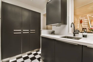 Görüntünün ortasında siyah dolaplar ve beyaz tezgahlı bir mutfak bir fırın, bulaşık makinesi ve lavabo.