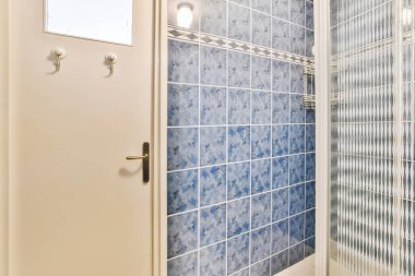 Duvarlarında mavi ve beyaz fayanslar olan bir banyo, duş kabini kapısı açık.