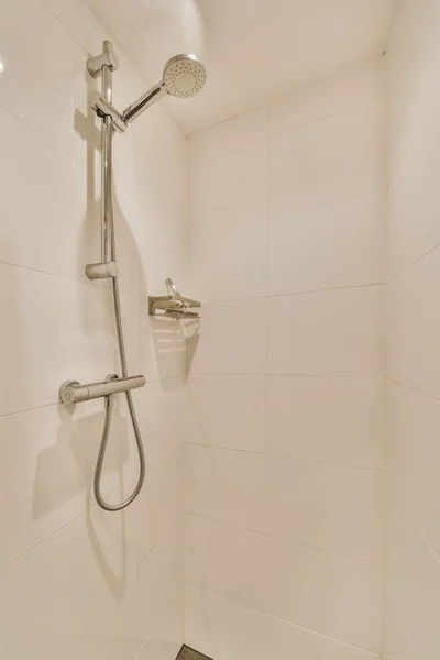 a shower in a white tiled bathroom with black tile flooring and wall mounted fauced on the walls