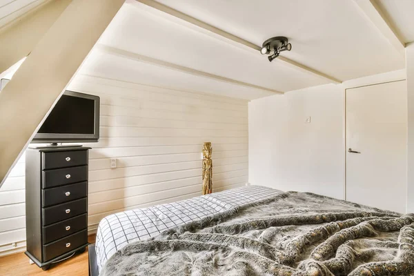 a bed in a room with white walls and wood flooring on the wall, there is a flat screen tv mounted above it