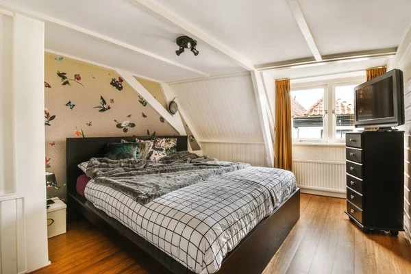 a bedroom with a bed, dressers and tv in the corner on the wall above the bed is an image of birds flying