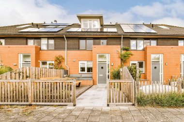 Çatıda güneş panelleri olan tuğladan bir ev ve ön bahçesinde mavi gökyüzü arka planında büyüyen bitkiler.