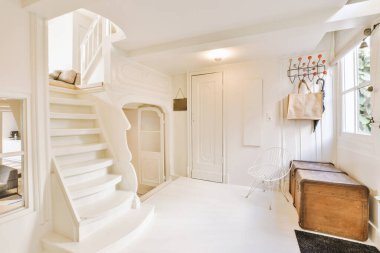 İkinci kata çıkan merdivenleri olan beyaz bir oda ve başka bir odaya açılan açık bir kapı.