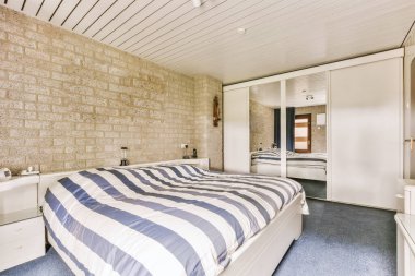 Arkasında yatak odası, şifonyer ve ayna olan bir yatak odası beyaza boyanmış bir tuğla duvardır.