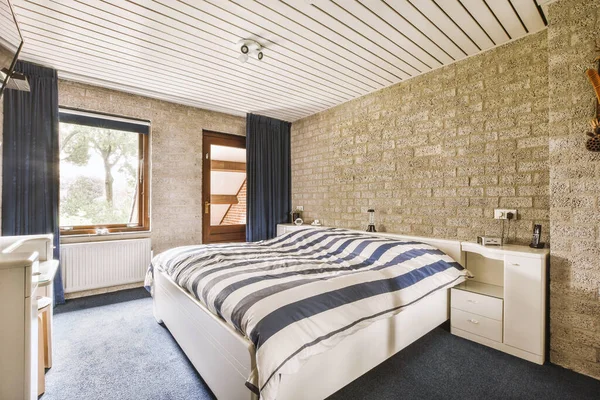a bedroom with a brick wall and blue rugs on the floor in front of the bed, next to a window