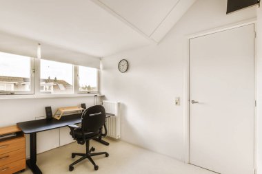 Masası, sandalyesi ve bilgisayarı olan bir oda şehre bakan bir pencerenin önünde.