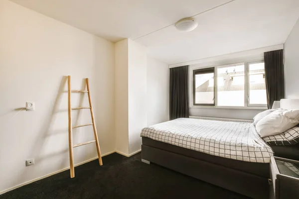 a bedroom with a ladder leaning against the wall in front of the bed and black carpet on the floor next to the window