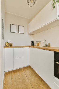 Üzerinde beyaz dolaplar ve ahşap tezgahlar olan bir mutfak. Bir fırın, lavabo, bulaşık makinesi, mikrodalga fırın.