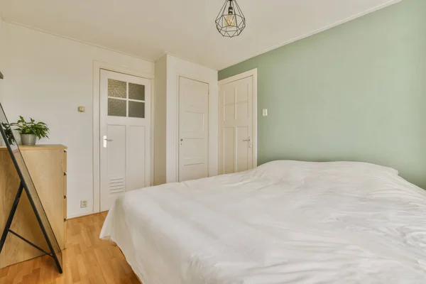 a bedroom with green walls and white bedding, wooden flooring and an open door leading to another room