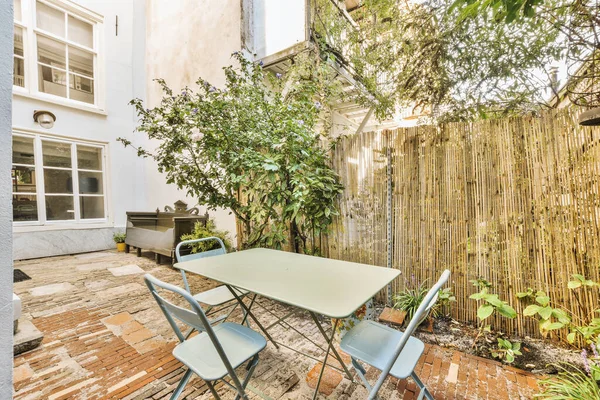 an outdoor patio with table and chairs in the back yard, next to a bamboo fence that has been used for several years