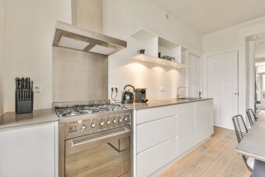 Metal mobilyalarla dolu yemek odası beyaz bir mutfağın yanında.