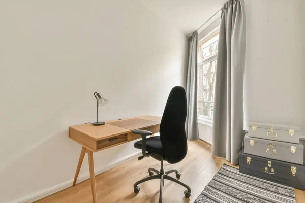 A small work area with a wooden table and an ergonomic chair next to the window