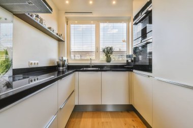 Odanın ortasında ahşap döşeme ve siyah tezgah ve beyaz dolaplarla dolu modern bir mutfak.