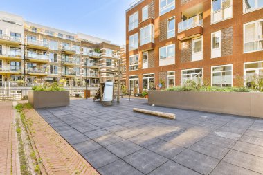 Parlak güneşli bir günde, ön planda bitki ve ağaçların olduğu bir apartman kompleksi.