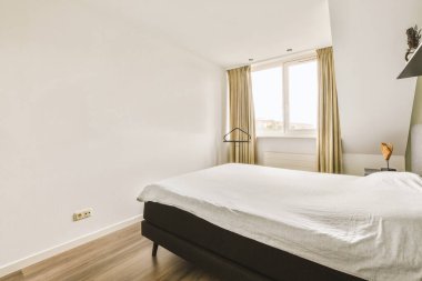 Beyaz duvarları ve ahşap döşemeleri olan bir yatak odası. Odada büyük bir yatakla birlikte duvarda bir tablo var.