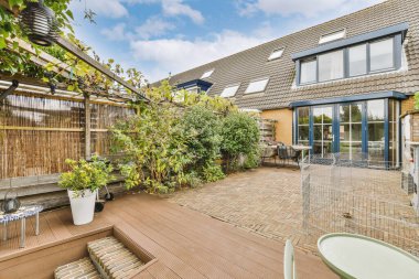 Arka bahçesinde ahşap döşeme ve yeşil bitkiler olan açık havadar bir evin önünde