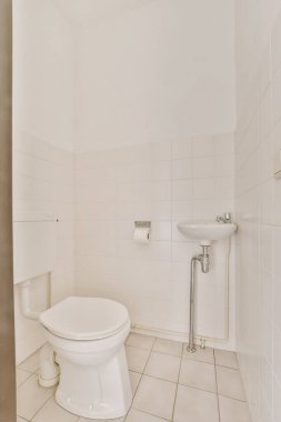 Duvarlarında ve zemininde beyaz fayanslar olan bir banyo. Odanın ortasındaki tuvalet de dahil.