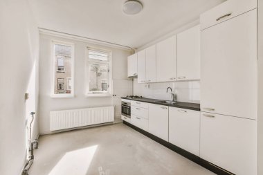 Boş bir odada beyaz dolapları ve siyah tezgahları olan bir mutfak. Sokağa bakan bir pencerenin yanında.