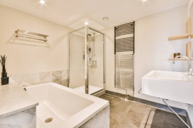 Modern bir banyo mermer döşemeli ve duşta büyük beyaz bir küvet lavabonun yanında.