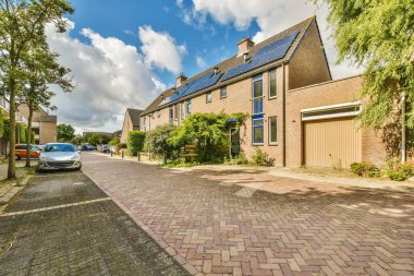 Çatıda güneş panelleri olan bir ev ve yanında park edilmiş iki araba ağaçlarla çevrili.