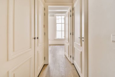 Beyaz duvarları ve yan yana ahşap döşemeleri olan uzun bir koridor diğer odalara açılıyor.