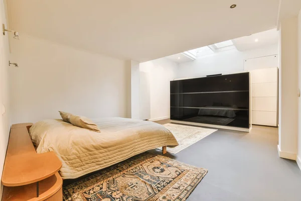 a bedroom with an area rug on the floor and a large bed in front of the wall mounted flat screen tv