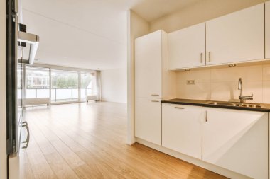 Beyaz dolapları ve siyah tezgahları olan bir mutfak. Oturma odasına açılan açık bir kapının önünde.