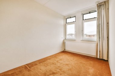 Pencerenin önünde iki penceresi ve yerde halısı olan bir oda sokağa bakıyor.