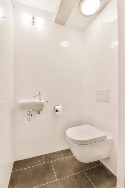 a bathroom with white walls and tile flooring, including a toilet in the center of the photo is a wall mounted mirror