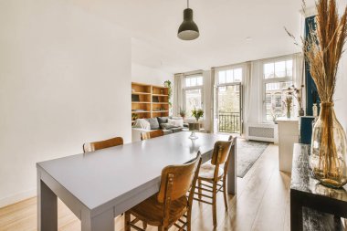 Ahşap döşemeleri ve beyaz duvarları olan bir yemek odası pencerenin önünde ahşap bir masa var.