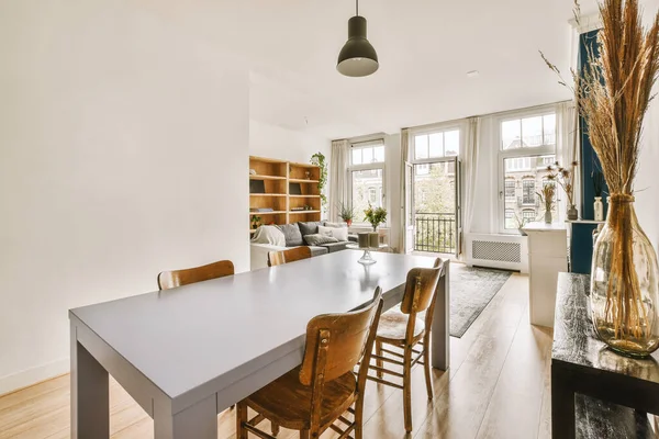 Ahşap döşemeleri ve beyaz duvarları olan bir yemek odası pencerenin önünde ahşap bir masa var.