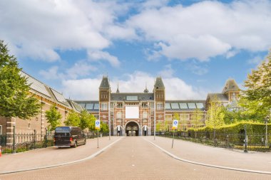 Caddenin ortasında büyük bir bina. Her iki tarafında ağaçlar ve üzerinde mavi bir gökyüzü var.