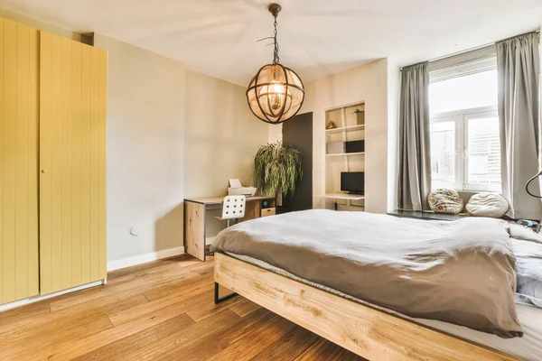 a bedroom with wood flooring and yellow painted closets on the wall behind it is a bed in front of a large window