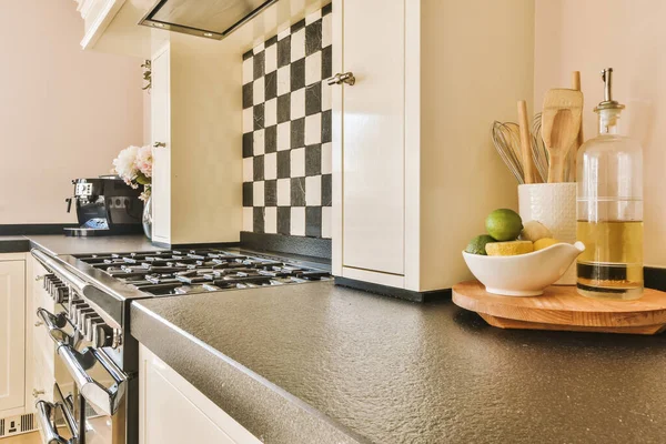 a kitchen with black and white tiles on the counter tops, along with a wooden cutting board next to the stove