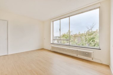 Ahşap zemin ve geniş pencereli boş bir oda içeriden çekilmiş şehir manzarası fotoğrafına bakıyor.