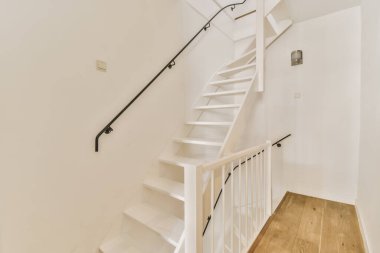 Merdivenlerde ahşap döşeme ve ahşap korkuluklar olan bir evde ikinci kata çıkan beyaz bir merdiven.