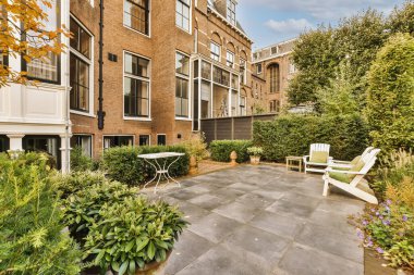 Ağaçlarla çevrili tuğla bir binanın önünde bazı bitki ve çiçeklerin bulunduğu bir alan.