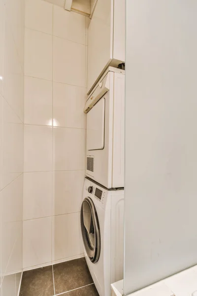 a white washer and dryer in a small room with tile flooring on the walls, there is a mirror above it