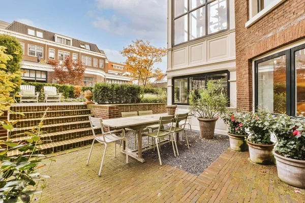 a patio area with chairs, tables and potted plants on the side of the house there is a brick wall in the background