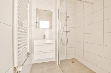 Beyaz fayanslı duvarları ve zemini olan modern bir banyo, sağ taraftaki duş kabininde yürümek de dahil.