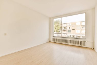 Beyaz duvarları ve ahşap döşemeleri olan boş bir oda. Odada penceresi olmayan büyük bir pencere var.