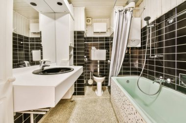 Duvarlarında siyah beyaz fayanslar olan bir banyo küvet, tuvalet, lavabo ve küvet.