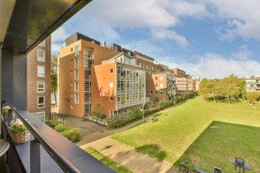 Fotoğrafta bazı binalar ve yeşil çimenler olan bir dış alan bir balkondan sokağa bakıyor.