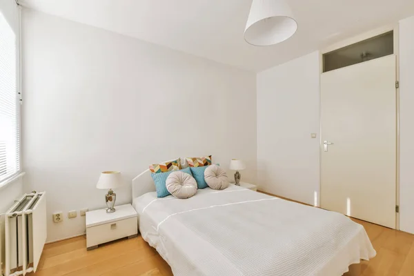 a bedroom with white walls and hardwood flooring in the room, it has a large bed that is next to the window