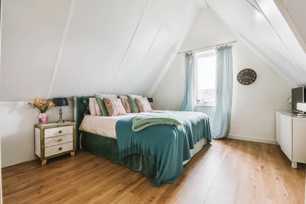 a bedroom with wood floors and white walls, including a bed in the corner of the room has a green blanket on it