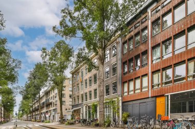 Kaldırımlarda bisikletleri ve arka planda binaları olan bir şehir caddesi var. Bulutlu mavi bir gökyüzü var.